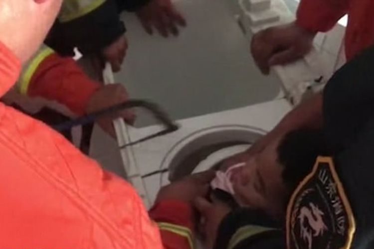 Petugas dari dinas pemadam kebakaran bersama kepolisian berusaha mengeluarkan seorang bocah berusia empat tahun yang terjebak di dalam mesin cuci.
