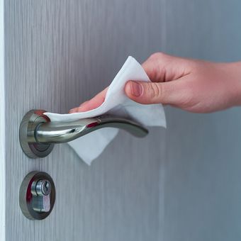 Ilustrasi membersihkan gagang pintu dengan tisu basah antibakteri. 