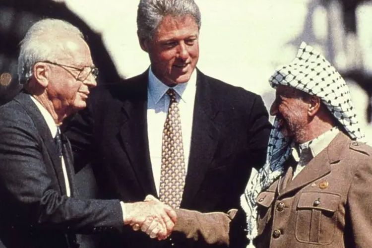 Presiden Amerika Bill Clinton menyaksikan Perdana Menteri Israel Yitzhak Rabin berjabat tangan dengan pemimpin Palestina Yasser Arafat di Gedung Putih setelah penandatanganan kesepakatan yang mengalihkan sebagian besar Tepi Barat ke kendali Palestina.