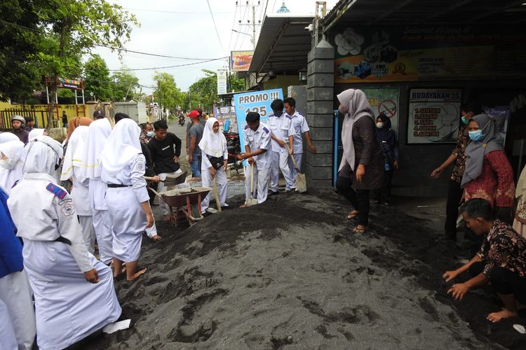 Siswa SMK WYSN Lumajang membersihkan tumpukan pasir yang menutupi gerbang sekolah, Jumat (27/5/2022)