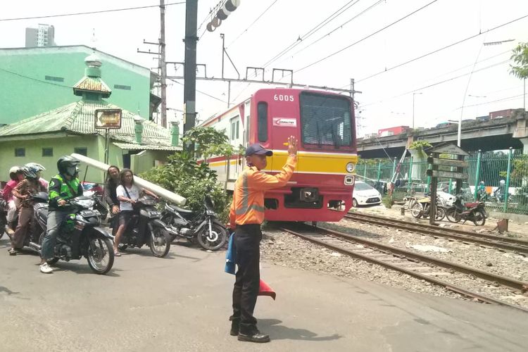 Petugas memberi tanda agar kendaraan berhenti saat kereta melewati di perlintasan kereta api yang berada di sekitar Stasiun Ancol, Jakarta, Rabu (4/12/2019). petugas PJL harus selalu siaga sebab mereka bertugas menjaga perlintasan karena ketiadaan palang pintu kereta api otomatis. 