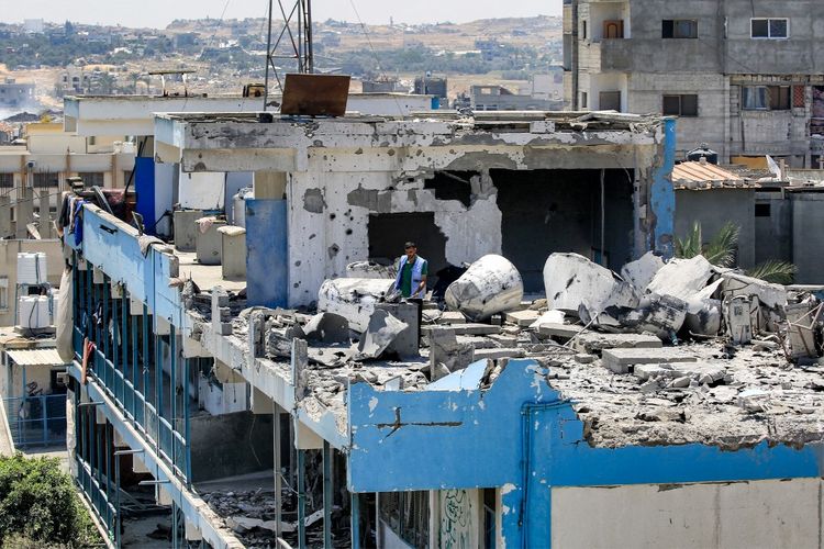 Seorang pekerja Badan Bantuan dan Pekerjaan PBB untuk Pengungsi Palestina (UNRWA) memeriksa kerusakan di atap sekolah yang dikelola UNRWA yang sebelumnya dihantam oleh pemboman Israel di kamp Nuseirat di Jalur Gaza tengah pada 7 Juni 2024 di tengah konflik yang sedang berlangsung di wilayah Palestina antara Israel dan Hamas. 