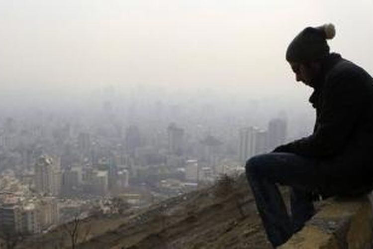Seorang warga kota Teheran, Iran duduk di atas sebuah bukit, sementara di bawahnya pemandangan kota nampak diselimuti polusi. Polusi udara di kota Teheran sudah mencapai tahap berbahaya sehingga membuat sejumlah sekolah terpaksa ditutup.