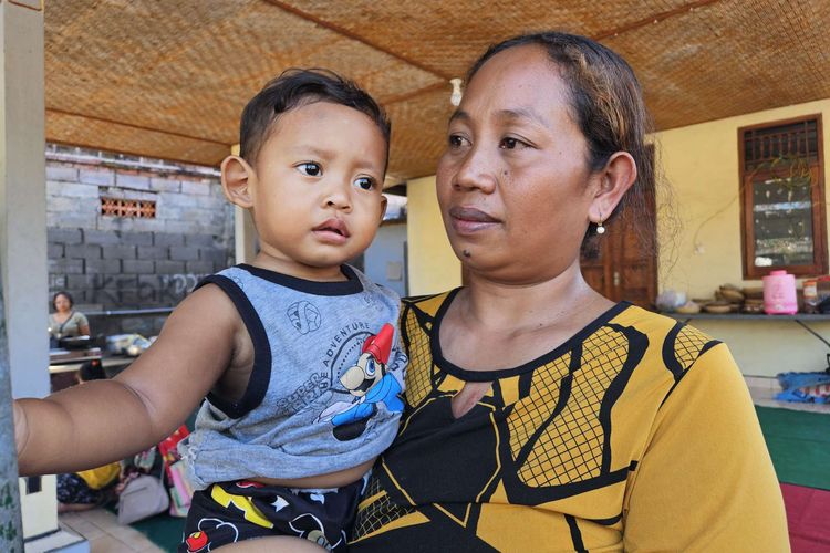 Kadek Sudiartini (38) menggendong putra bungsunya, Kamis (10/7/2025) di Buleleng, Bali. Sudiartini merupakan istri Putu Mertayasa (43), salah satu korban tenggelamnya KMP Tunu Pratama Jaya.
