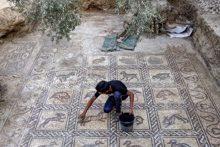 Putra petani Palestina Salman al-Nabahin menggunakan spons untuk mengungkap mosaik Bizantium yang berasal dari abad kelima hingga ketujuh setelah ditemukan oleh ayahnya saat membajak tanahnya di Bureij di Jalur Gaza tengah pada 18 September 2022. 