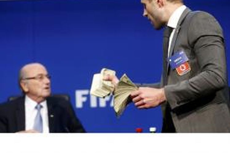 Komedian Inggris, Simon Brodkin, maju ke podium sebelum melempar Sepp Blatter dengan ratusan lembar uang dollar AS palsu.