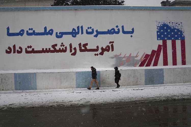 Orang-orang berjalan melewati tembok dengan slogan bertuliskan: Dengan pertolongan Tuhan, bangsa kita mengalahkan Amerika, di Kabul, Afghanistan, Minggu, 6 Februari 2022.