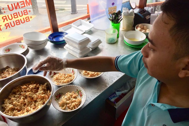 Seorang karyawan menyiapkan bubur ayam telur untuk pelanggan di Bubur Cikini