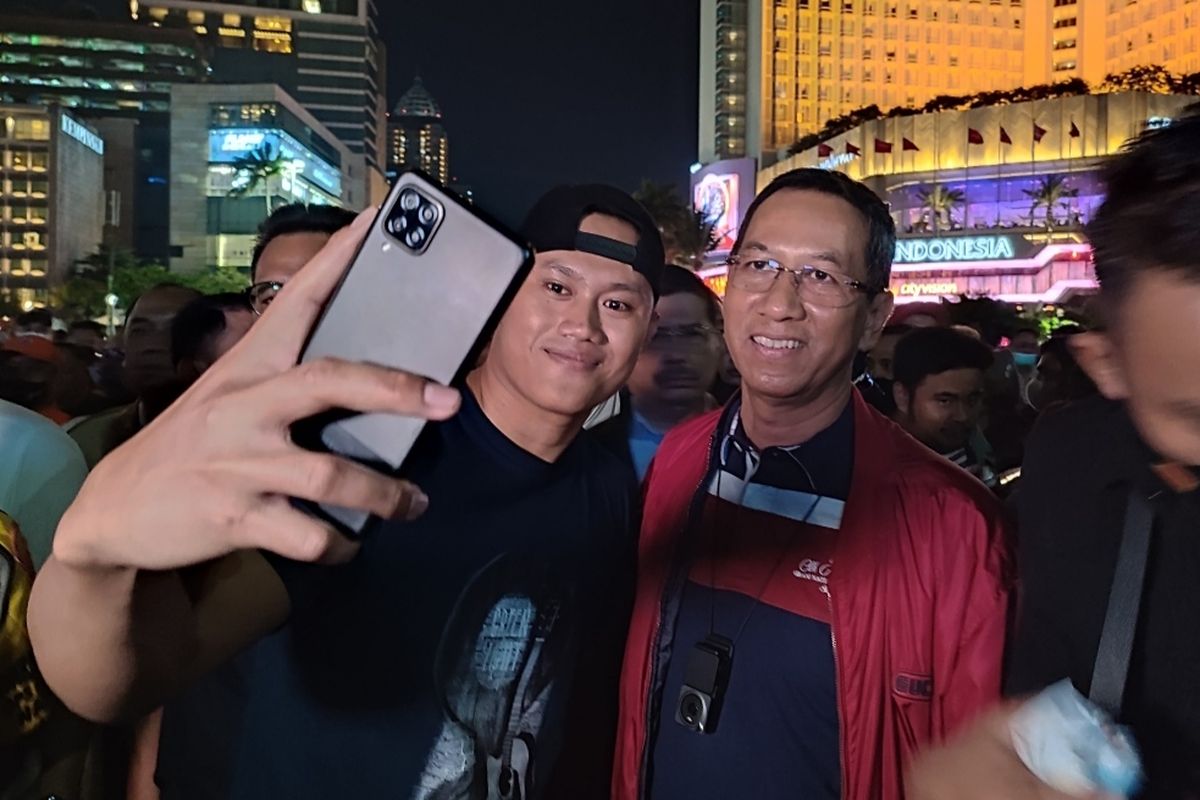 Penjabat (Pj) Gubernur DKI Jakarta Heru Budi Hartono turut meramaikan perayaan malam pergantian tahun 2023 dengan mendatangi kawasan Bundaran Hotel Indonesia (HI), Sabtu (31/12/2022). Heru diajak selfie warga.
