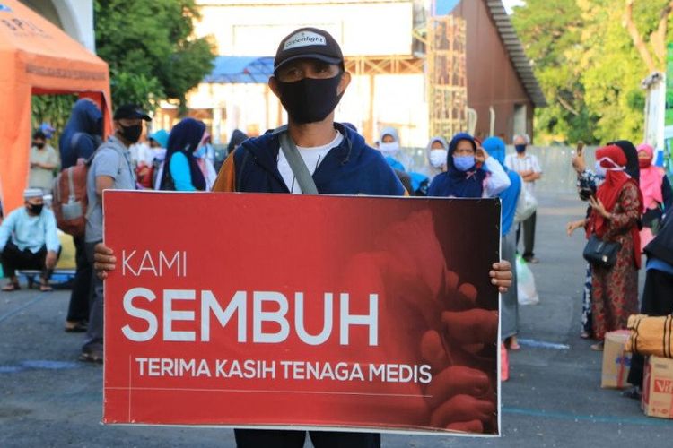 Seorang warga yang dinyatakan sembuh dari Covid-19 membawa spanduk bertuliskan ucapan terima kasih kepada tenaga medis saat dipulangkan dari tempat karantina di Asrama Haji Surabaya, Jumat (5/6/2020).