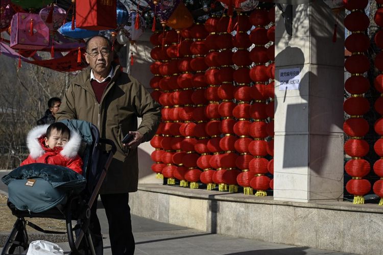 Seorang pria yang mendorong troli bayi berjalan melewati lentera yang dihias di sebuah pusat perbelanjaan di Beijing pada 4 Februari 2023. Banyak RS di China dilaporkan kini telah menyetop layanan persalinan karena menurunya tingkat kelahiran.