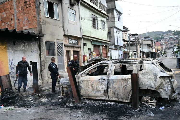Petugas polisi berdiri di samping mobil yang terbakar yang merupakan bagian dari barikade yang didirikan selama Operacao Contencao (Operasi Penahanan) di favela Vila Cruzeiro, di kompleks Penha, di Rio de Janeiro, Brasil, pada 28 Oktober 2025. Ratusan polisi Brasil yang bersenjata lengkap menyerbu daerah kumuh Rio dalam penggerebekan narkoba pada hari Selasa, memicu baku tembak yang disamakan dengan adegan perang dan menewaskan sedikitnya 64 orang, kata pejabat Brasil.