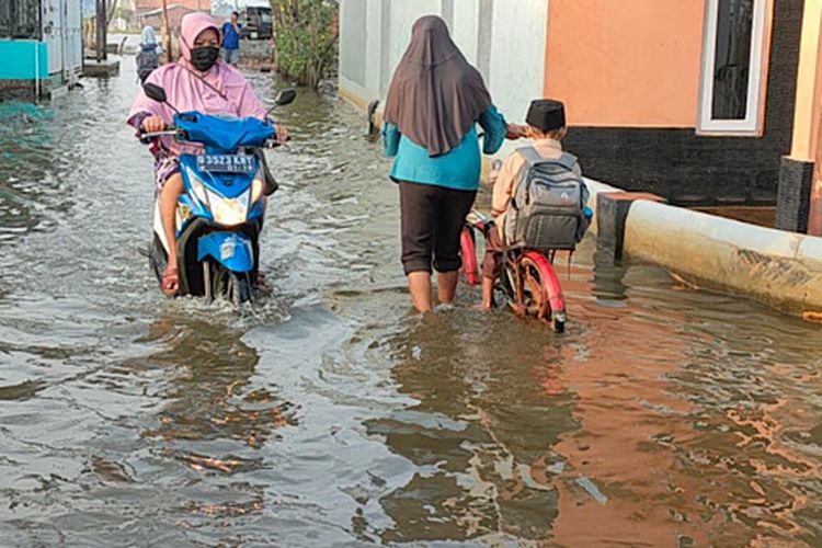 Warga melintas di akses jalan yang tergenang banjir di Kelurahan Degayu, Kota Pekalongan Jawa Tengah.