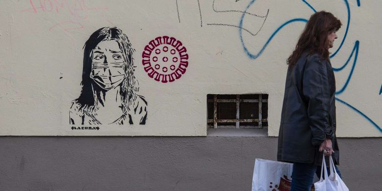 Pejalan kaki melintas di depan grafiti yang menampilkan seorang wanita mengenakan masker di Berlin, Jerman, 31 Maret 2020. Pandemi Covid-19 yang disebabkan oleh virus corona menjadi insipirasi seniman grafiti untuk memberikan peringatan dan motivasi bagi warga dalam menghadapi virus tersebut.