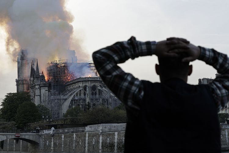 Warga menyaksikan api membakar bagian atas Gereja Notre Dame di Paris, Perancis, pada Senin (15/4/2019). Belum diketahui penyebab pasti kebakaran itu, api dengan cepat melalap atap dan puncak menara gereja bernuansa Gotik yang dibangun pada abad ke-12 itu.