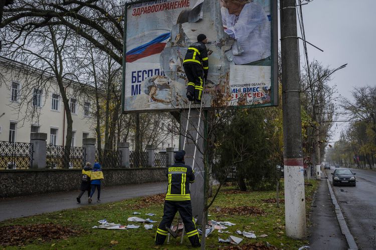 Petugas pemadam kebakaran melepas poster Rusia di Kherson, di selatan Ukraina, pada Kamis, 17 November 2022.