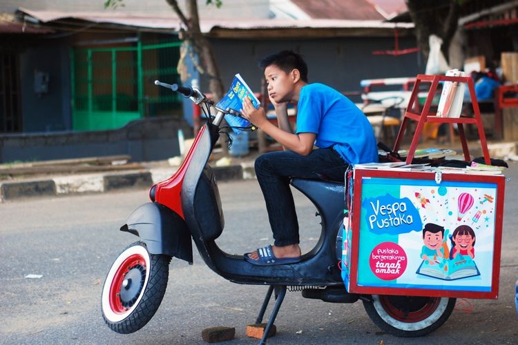 Seorang anak sedang membaca buku di kawasan Sebrang Pabayan, tepi Sungai Batang Arau, Padang, Sumatera Barat, Minggu (16/7/2017). Komunitas Baca Tanah Ombak meluncurkan kegiatan pustaka bergerak yang diberi nama Vespa Pustaka untuk menjangkau anak-anak di Kota Padang yang membutuhkan akses pendidikan lewat buku.