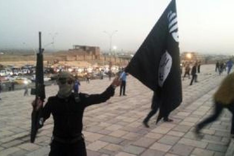 Seorang pejuang Negara Islam (ISIS) memegang bendera ISIS dan senjata di Mosul, Irak.