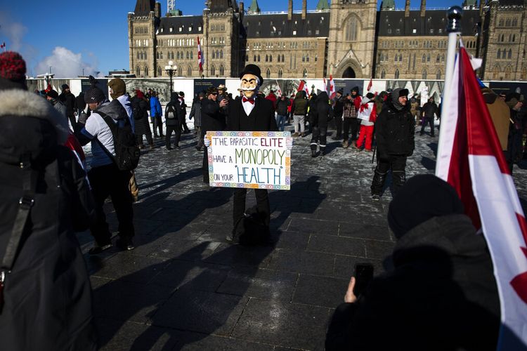 Seseorang yang mengenakan topeng Monopoly Man memegang poster selama demonstrasi menentang pembatasan COVID-19 di Parliament Hill, yang dimulai sebagai konvoi lintas negara yang memprotes mandat vaksin federal untuk pengemudi truk, di Ottawa, pada Sabtu, 29 Januari 2022.