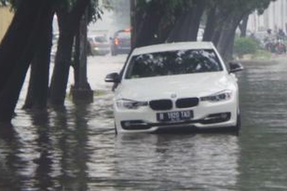 Diduga mogok karena banjir, sedan BMW bernomor polisi B 1920 TAD berwarna putih terjebak di tengah banjir yang menggenangi Jalan Bulevard Barat, Kelapa Gading, Jakarta Utara, Jumat (23/1/2015).