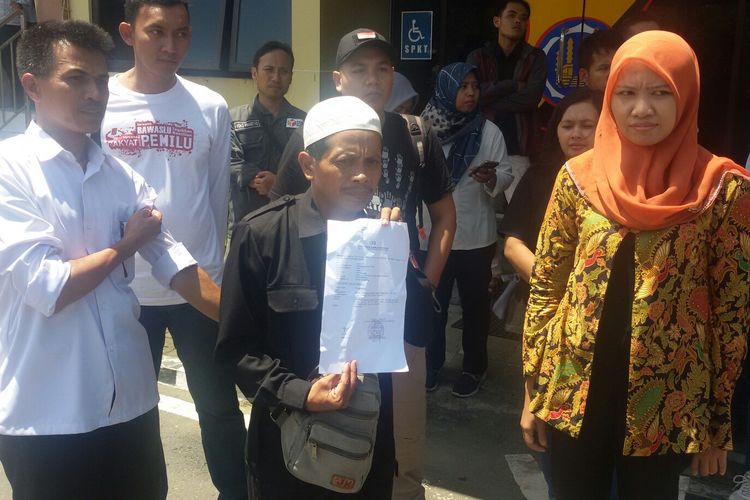 Panwas Desa Sentolo Janarta (46), sambil mengenakan kopiah putih, melaporkan kasusnya ke Polres Kulon Progo, DIY. Dengan ditemani Ketua Bawaslu Kulon Progo, Ria Harlinawati, dan belasan anggota Panwas tingkat kecamatan.