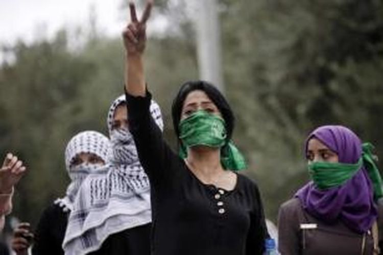 Perempuan Palestina, dengan menutup mulut menggunakan syah Hamas, emngacungkan tanda victory saat bentrokan dengan tentara Israel di Beit El, dekat ramalla, Tepi Barat, 10 Oktober 2015.