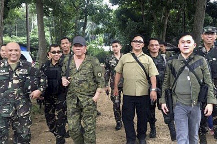 Presiden Filipina, Rodrigo Duterte (kiri tengah) mengenakan topi dan membawa senapan, berjalan bersama anggota tentara.
