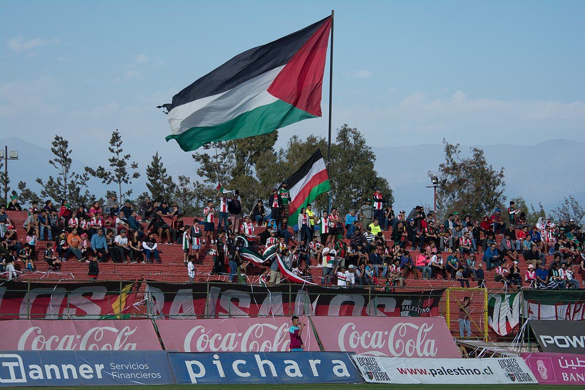 Penonton Palestino mengibarkan bendera Palestina
