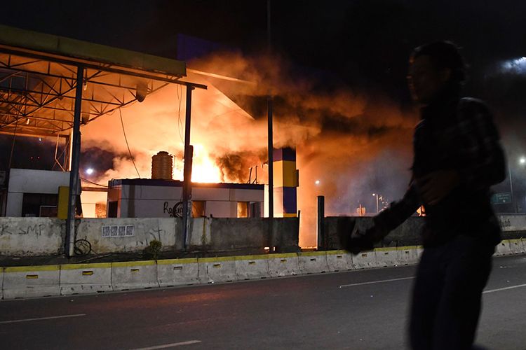 Warga melintasi Gerbang Tol Pejompongan yang dibakar massa, di Jakarta, Selasa (24/9/2019). Demo mahasiswa yang berlangsung di depan Gedung DPR sejak tadi pagi berakhir ricuh, suasana tidak kondusif terjadi sejak sore hingga malam hari.