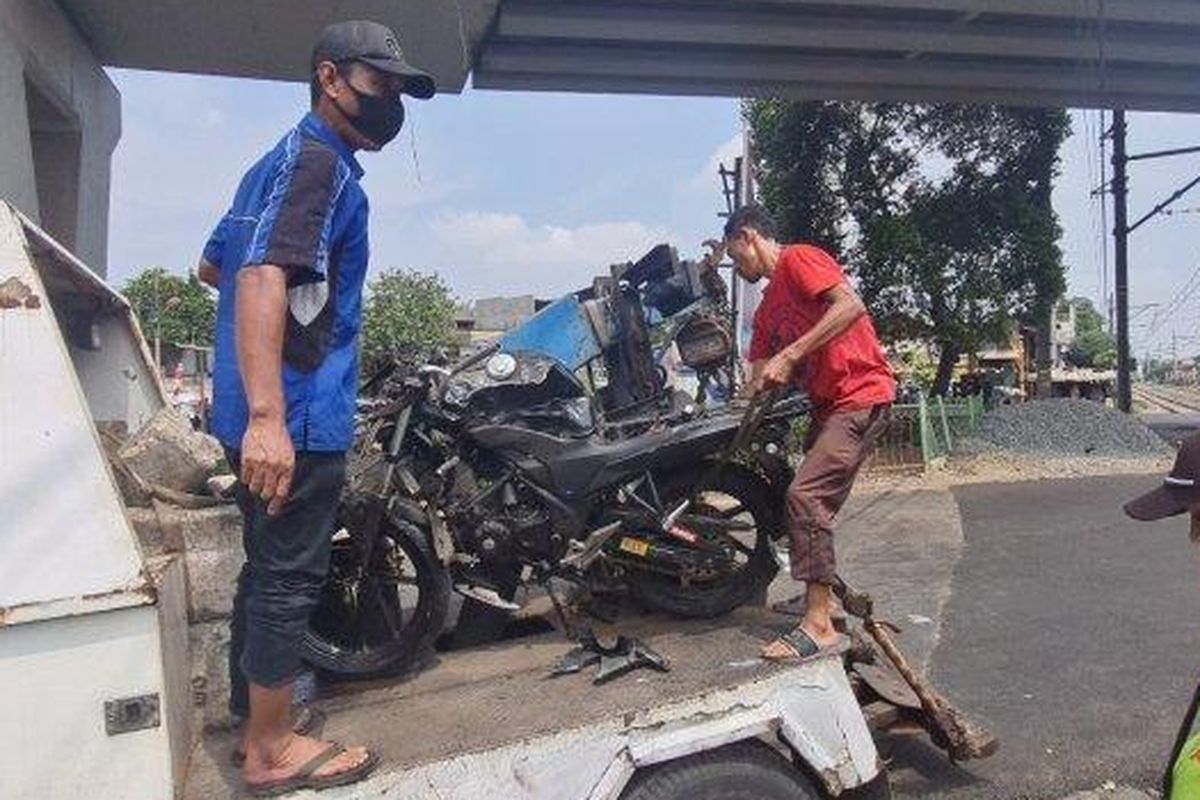 Sejumlah petugas mengangkut motor sport yang ringsek usai ditabrak kereta bandara di pintu perlintasan rel kereta di Pesing, Grogol Petamburan, Jakarta Barat pada Selasa (16/8/2022). 
