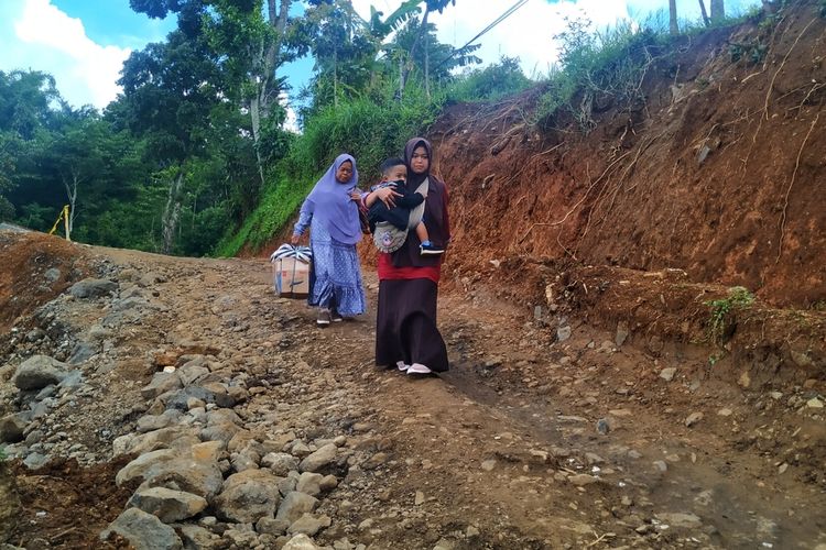 Dua penumpang angkutan umum terpaksa berjalan kaki melintasi lokasi tanah bergerak untuk menyambung mobil lain di Kampung Gunungnatu, Desa Kertaangsana, Nyalindung, Sukabumi, Jawa Barat, Rabu (19/2/2020).