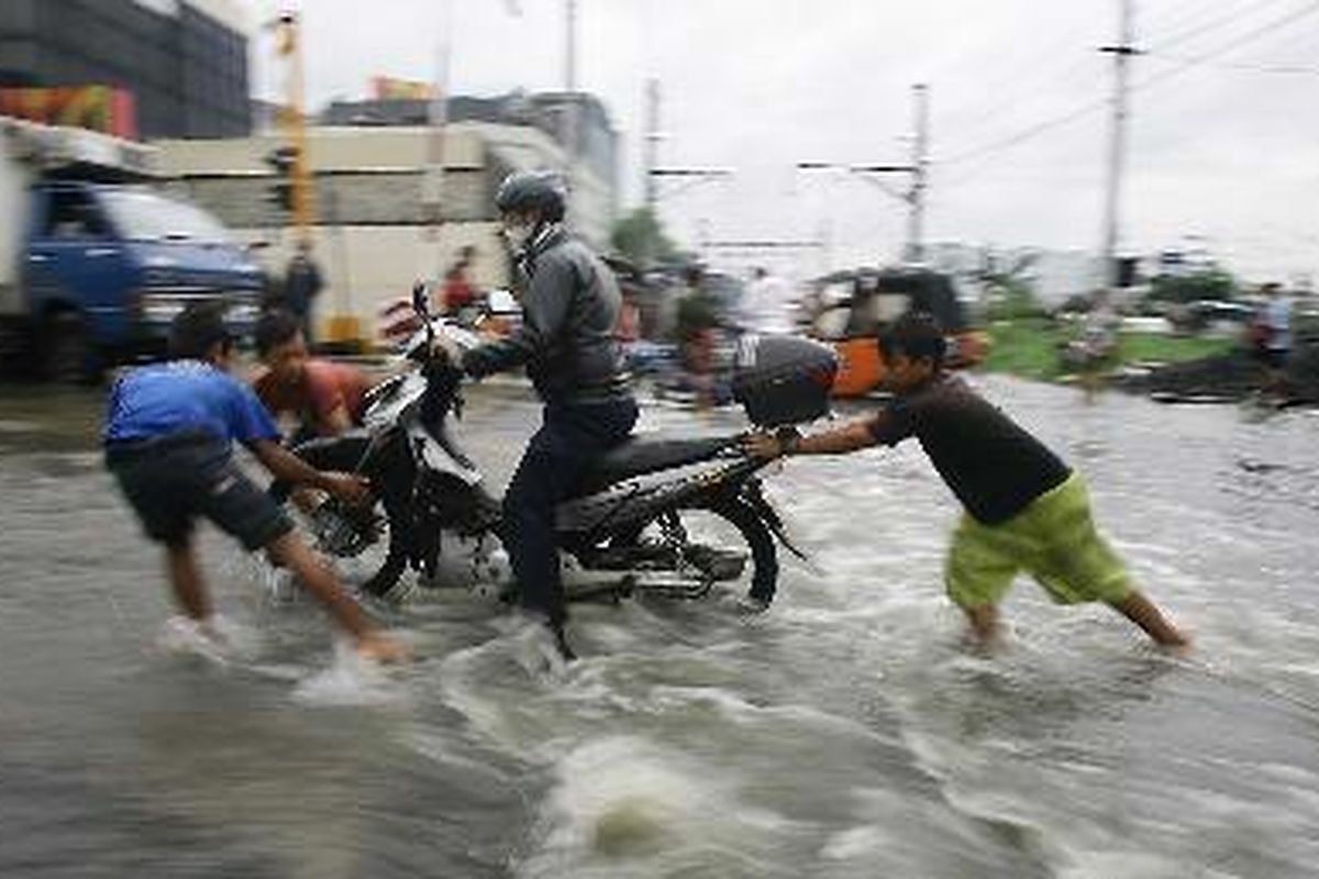 Anak-anak membantu sepeda motor yang terjebak di perlintasan kereta api di Kampung Bandan, Jakarta Utara, Jumat (4/1). Banyak pengguna jalan yang terjebak di perlintasan kereta api yang berlubang Jalan dan tertutup genangan air akibat hujan deras yang menguyur Jakarta beberapa hari terakhir.  kompas/lucky pransiska 4 januari 2008.