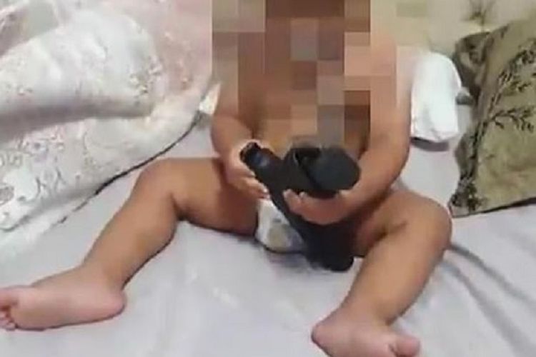 Rekaman video yang beredar di media sosial memperlihatkan bayi bermain dengan pistol sungguhan jenis Glock yang dikabarkan terisi peluru.