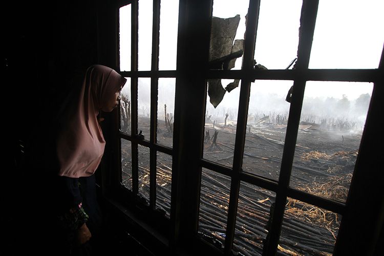 Warga melihat kebakaran lahan gambut dari balik jendela rumah di desa Pengayuan, Banjarbaru, Kalimantan Selatan, Sabtu (14/9/2019). Kebakaran lahan gambut di kawasan tersebut mengakibatkan satu tempat usaha warga dan sebagian dinding rumah warga ikut terbakar.
