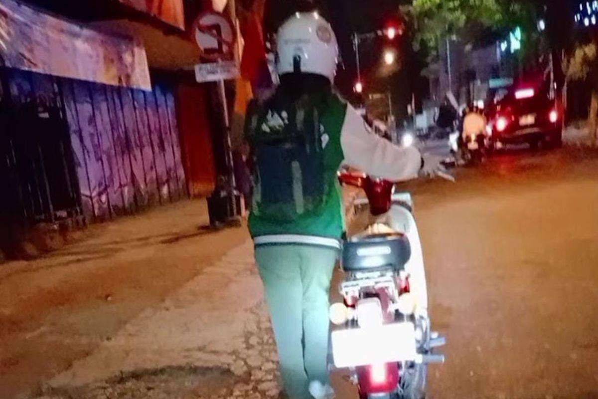 Seorang perempuan mendorong motor karena ban bocor