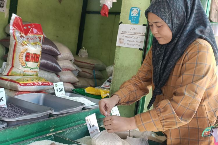 Pedagang beras di Pasar Perumnas Klender, Syahfitri Mariah (41), saat melayani seorang pembeli beras di lapak dagangannya di Pasar Perumnas Klender, Duren Sawit, Jakarta Timur, Senin (28/8/2023).