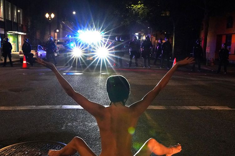 Seorang pengunjuk rasa perempuan dengan telanjang duduk menghadapi polisi, dalam demonstrasi menentang ketidaksetaraan ras di Portland, Amerika Serikat, pada 18 Juli 2020.