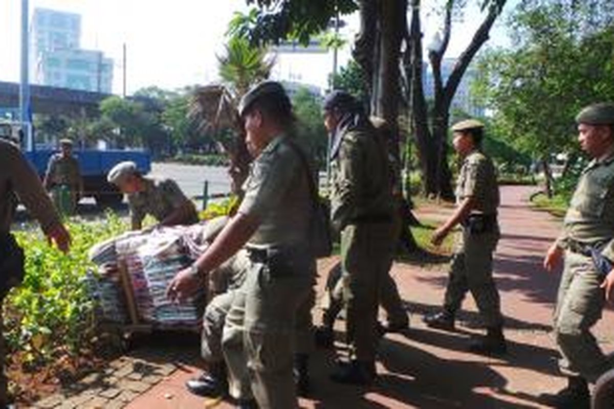 Petugas Satpol PP menyita barang dagangan dari PKL di Monas yang disembunyikan pedagang di semak taman. Sabtu (2/8/2014).