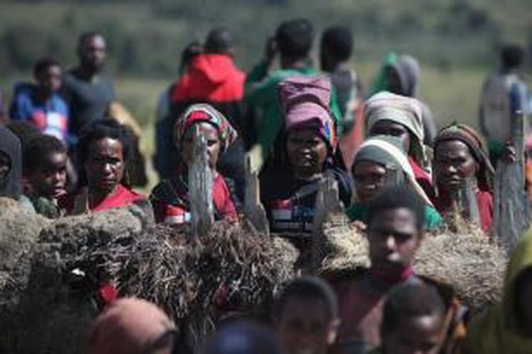 Warga menunggu pembagian bantuan makanan di balik pagar lapangan terbang Kuyawage, Lanny Jaya, Papua, Senin (27/7/2015). Cuaca ekstrem melanda sejumlah daerah di Papua. Kebutuhan obat-obatan, makanan kaleng dan pakaian masih disalurkan ke wilayah yang terkena dampak kelaparan.