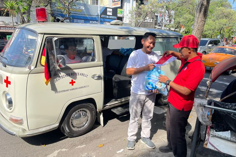 Salah satu anggota Volkswagen Jawa Timur membagikan sembako kepada tukang becak yang ditemui saat konvoi memperingati Hari Kemerdekaan RI ke-80 dan merayakan HUT Volkswagen Indonesia ke-32 di Surabaya, Sabtu (16/8/2025) siang.