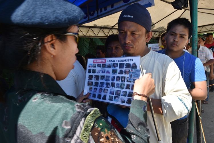 Polisi mencocokkan wajah warga dan komuter yang akan memasuki Iligan City di Mindanao dengan foto-foto terduga teroris untuk mencegah anggota kelompok militan yang menyerang kota Marawi menyelinap ke kota itu.