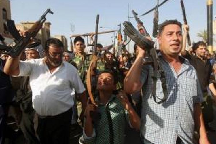 Seorang anak bersama para orangtua di Baghdad, mengangkat senjata saat berkumpul untuk menunjukkan kesiapan mereka bergabung dengan pasukan keamanan Irak dalam perang melawan militan Jihad yang telah mengambil alih beberapa kota di utara Irak, 16 Juni 2014.