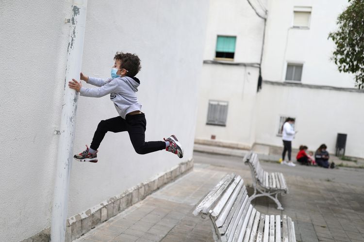 Kilian (6) yang mengenakan masker melompat dari bangku. Dia menjadi sekian banyak anak berusia di bawah 14 tahun di Spanyol yang diizinkan keluar pada Minggu (26/4/2020), sebagai bagian dari upaya pemerintah melonggarkan lockdown virus corona.