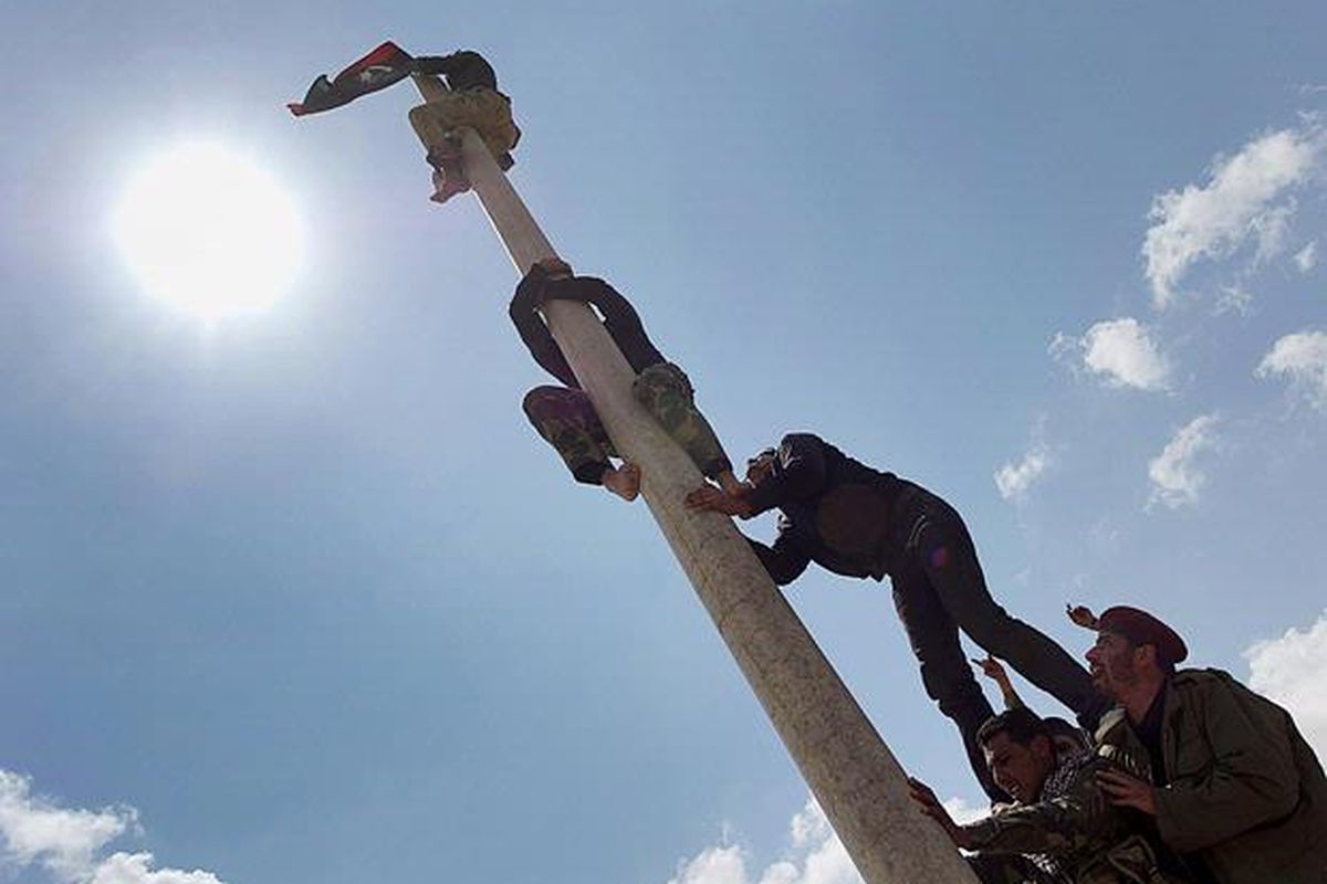 Anggota pasukan oposisi memanjat sebuah tiang untuk mengibarkan bendera oposisi di dekat kota  Brega, Libya, Minggu (3/4).