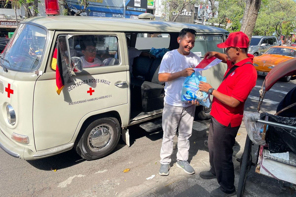 Salah satu anggota Volkswagen Jawa Timur membagikan sembako kepada tukang becak yang ditemui saat konvoi memperingati Hari Kemerdekaan RI ke-80 dan merayakan HUT Volkswagen Indonesia ke-32 di Surabaya, Sabtu (16/8/2025) siang.