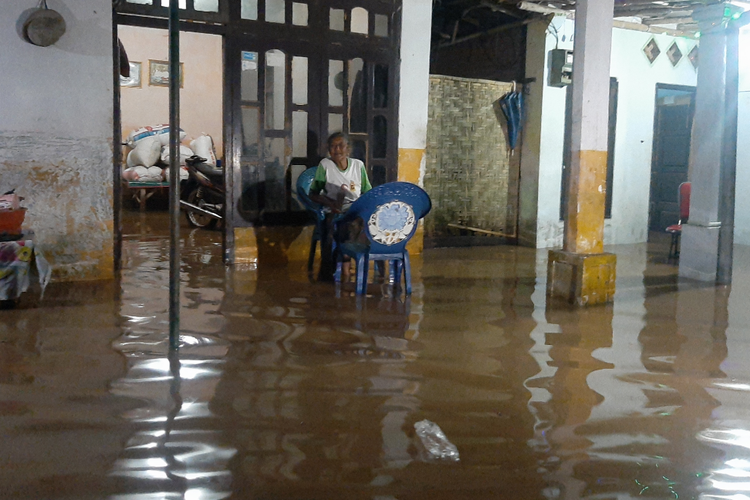 Nenek Sayati duduk didepan rumahnya memantau kondisi banjir yang merendam rumahnya sambil menjaga sang ibu, Selasa (15/3/2022) dinihari