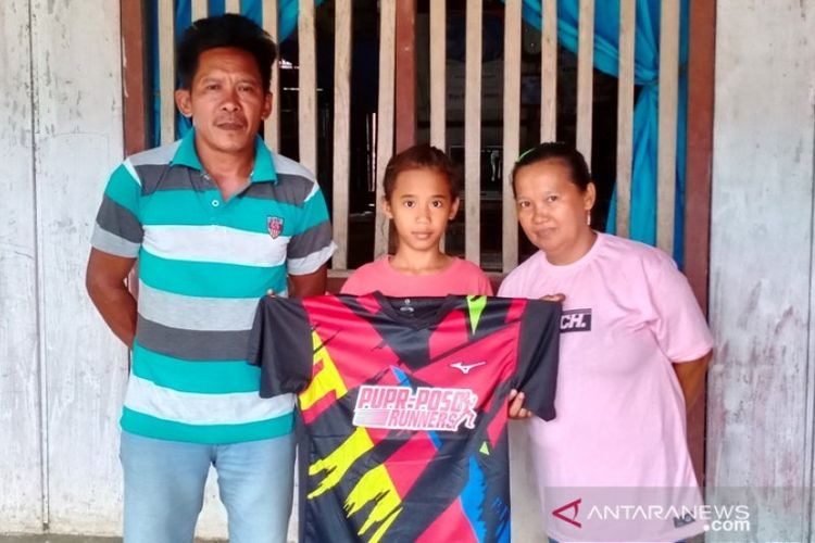 Asmarani (tengah) didampingi bapak dan ibunya di kediaman pribadi mereka di Desa Pandiri, Kecamatan Lage, Poso, memegang kaos hadiah dari Runner Poso, Rabu (29/1/2020).
