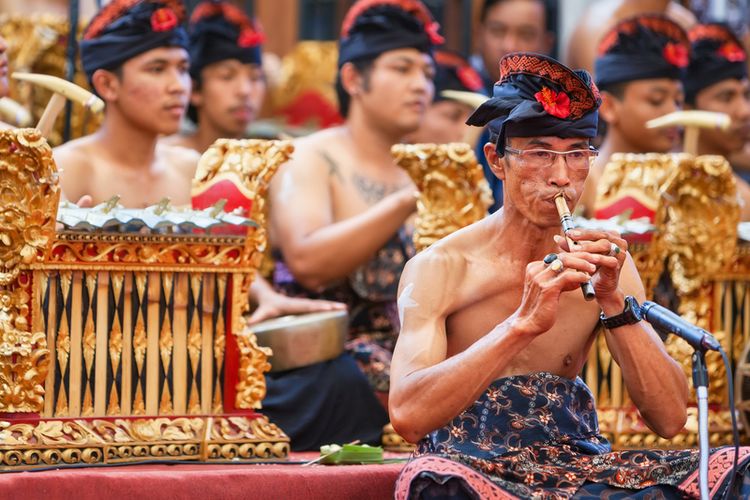 BALI, INDONESIA - JUNE 21, 2015: Old musician man of traditional Gamelan orchestra dressed in Balinese style male costume playing ethnic music on bamboo flute Suling at Art and Culture Festival.