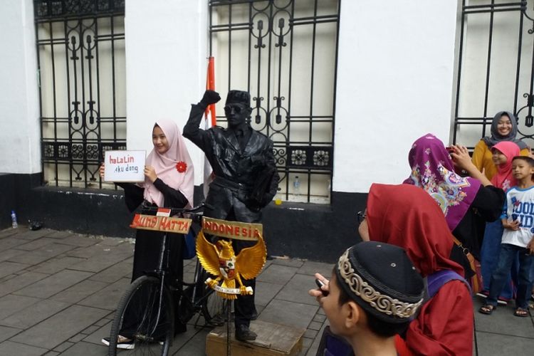 Seorang pengunjung membawa kertas bertulisan Halalin Aku Dong sedang berfoto dengan manusia patung di kompleks Museum Fatahillah, kawasan Kota Tua, Jakarta Barat, (30/6/2017).