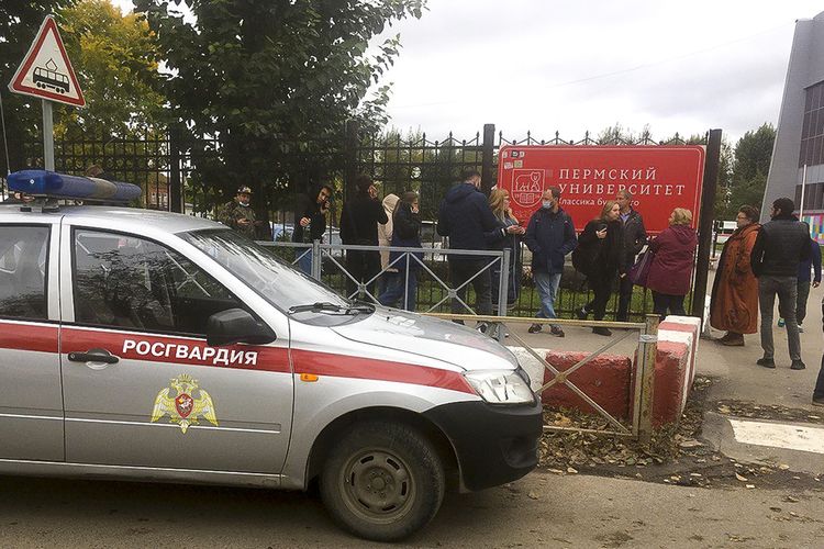 Orang-orang berdiri di belakang pagar Universitas Perm, Rusia, bersama garda nasional setempat pada Senin (20/9/2021). Seorang mahasiswa menembaki kampus tersebut pada Senin pagi yang menewaskan sedikitnya delapan orang dan melukai sejumlah korban.